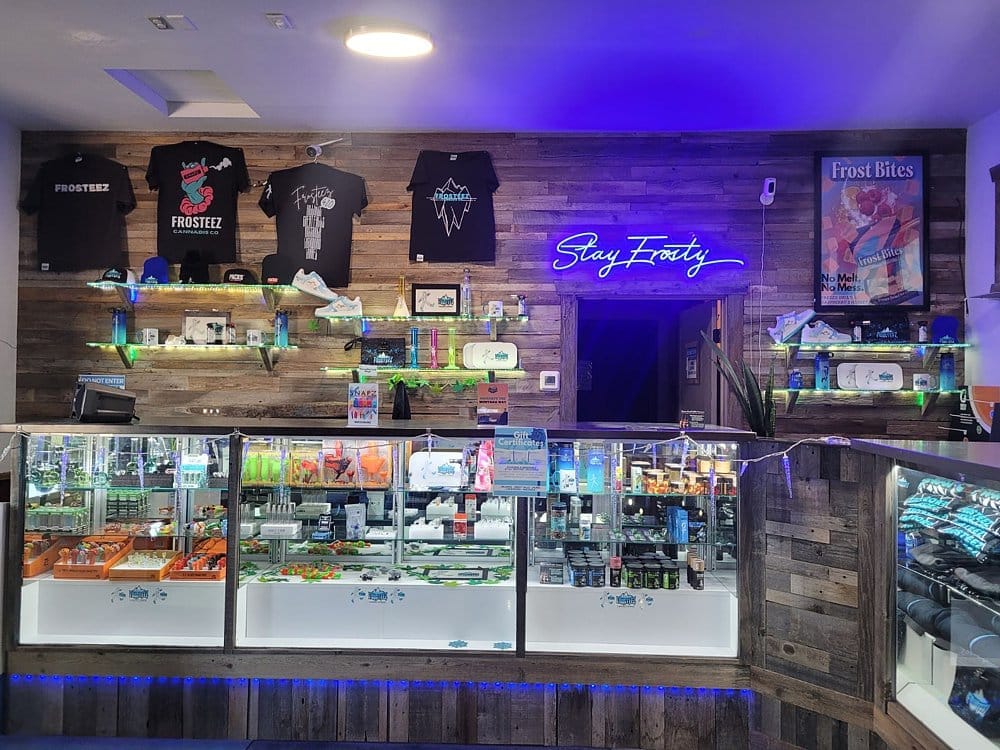 Frosteez Stay Frosty Neon Sign and Merch Display Frosteez dispensary Stay Frosty neon sign above the counter with branded merchandise and illuminated display cases
