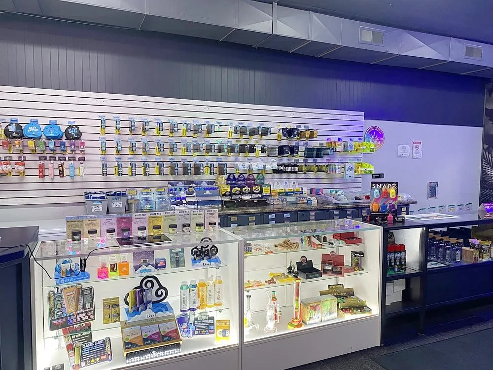 Interior of a vape shop with glass display cases full of devices and accessories, and wall shelves lined with various colorful packaging and chargers under cool blue lighting.